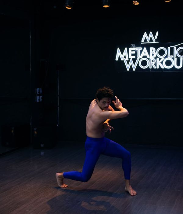 Man performing a complex balance and strength exercise in a dark studio.